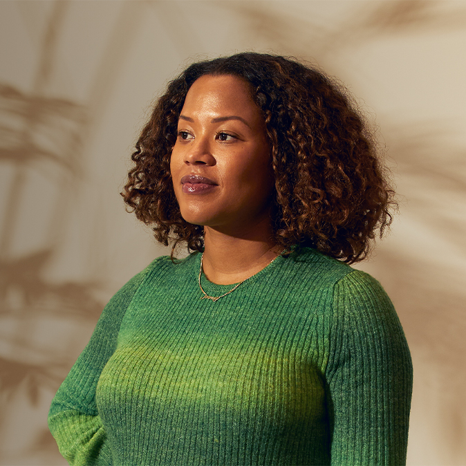 Sydney stoi w pomieszczeniu i spogląda w prawo. Na jej twarzy maluje się pewność siebie.