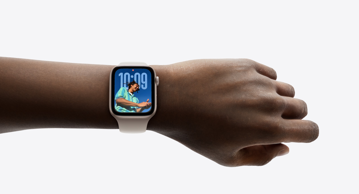 고무 밴드를 장착한 로즈 골드 마감의 Apple Watch가 손목에 착용된 이미지, 새로운 Liquid Glass 디자인의 시계 앱을 보여주는 모습