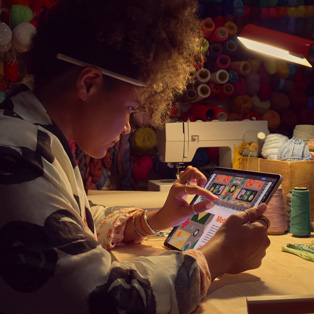 En person sitter vid ett skrivbord och zoomar in på en bild med två fingrar på en iPad.