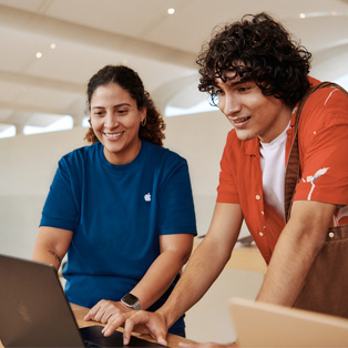 Apple Store employee standing next to a customer, both interacting with a MacBook.
