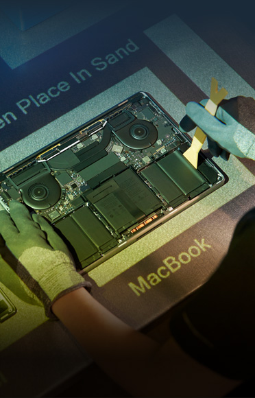 Dłonie w rękawicach demontują MacBooka, widoczne są jego wewnętrzne komponenty