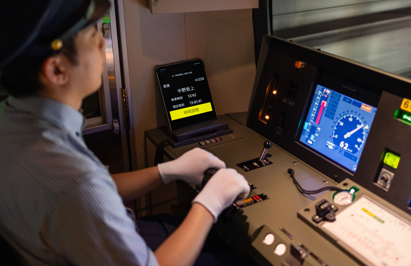 一部 iPad 螢幕顯示了停靠站與時刻 ，靜置於列車操作員執行作業的控制面板旁。