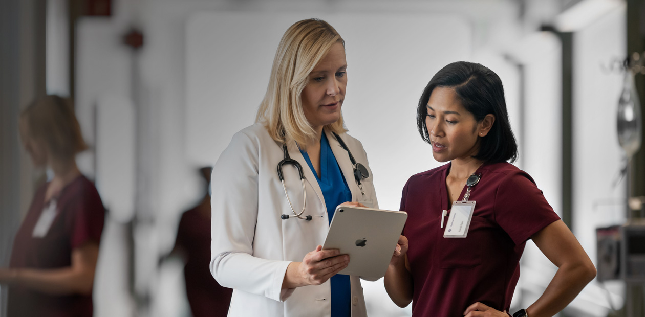 A physician and a nurse looking at an iPad together in a hospital hallway.