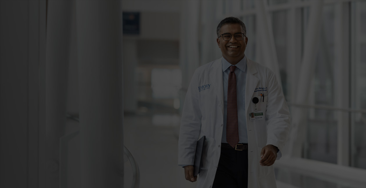  Ein Arzt, der beim Gehen ein MacBook unter dem rechten Arm trägt.