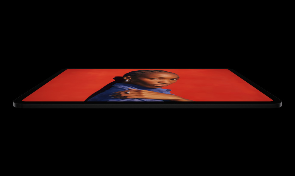 iPad Pro, side exterior, landscape orientation, space black colour, rounded corners, black display bezel, display showing a vibrant red screen with an individual posing with their hand on their shoulder wearing a blue shirt