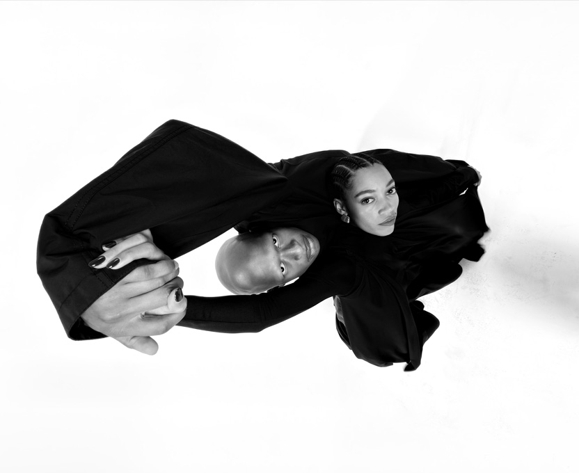 Melnā platleņķa fotogrāfijā redzamas divas personas, demonstrējot iPhone 17 Pro ultraplatleņķa kameras iespējas