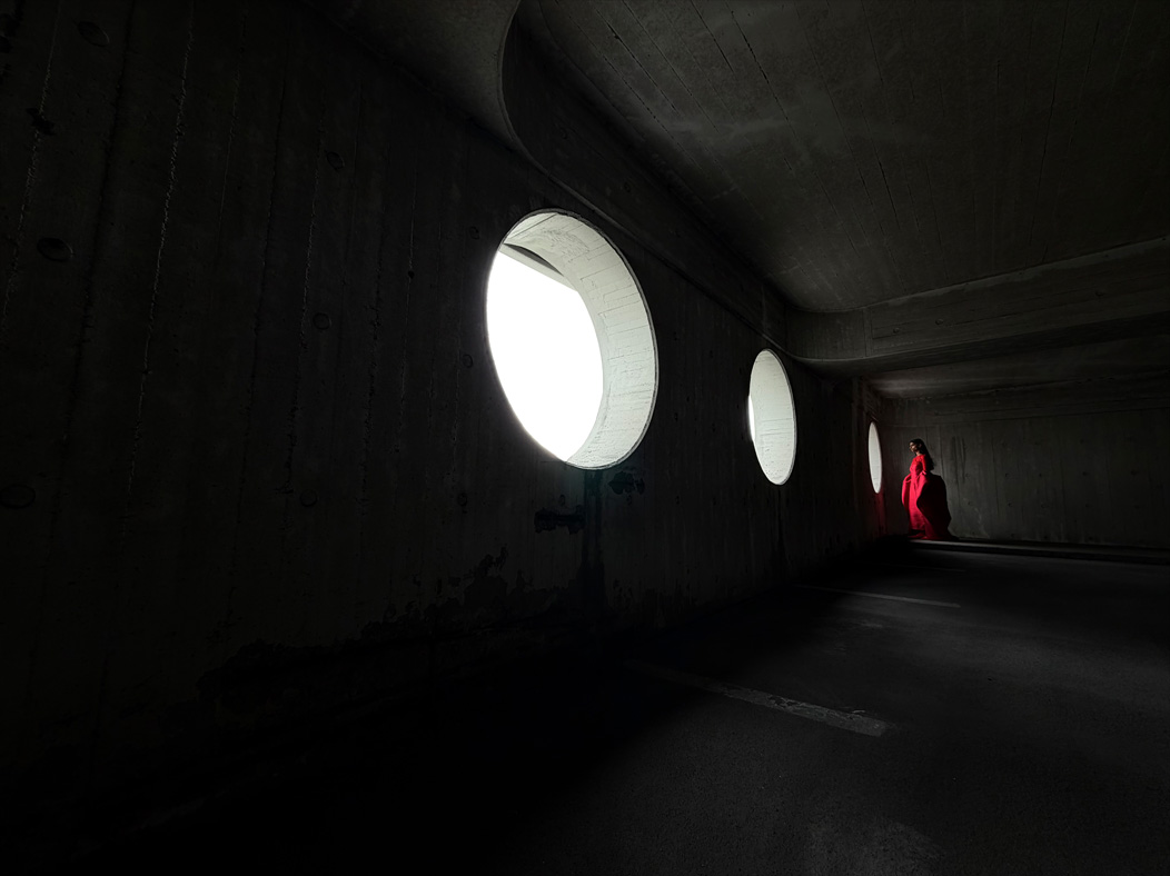 Uma mulher com um longo vestido vermelho a ser fotografada numa sala vazia. A app Fotografia muda de distância focal para ilustrar as capacidades do sistema de câmaras Pro, a mostrar a opção de 13 mm