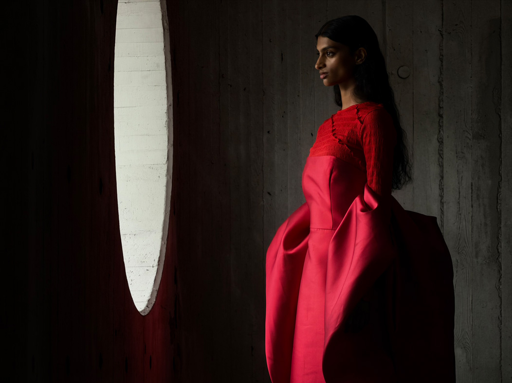 Uma mulher com um longo vestido vermelho a ser fotografada numa sala vazia. A app Fotografia muda de distância focal para ilustrar as capacidades do sistema de câmaras Pro, a mostrar a opção de 200 mm