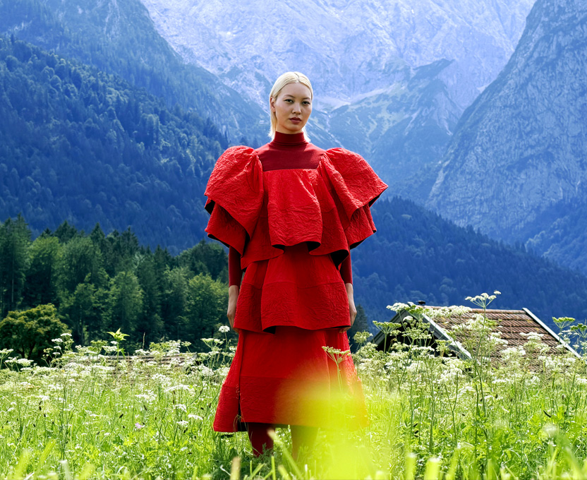 Une femme vêtue d’une robe rouge vif se tient debout dans une vallée de montagne, mettant en valeur la large gamme de couleurs du Studio Display XDR