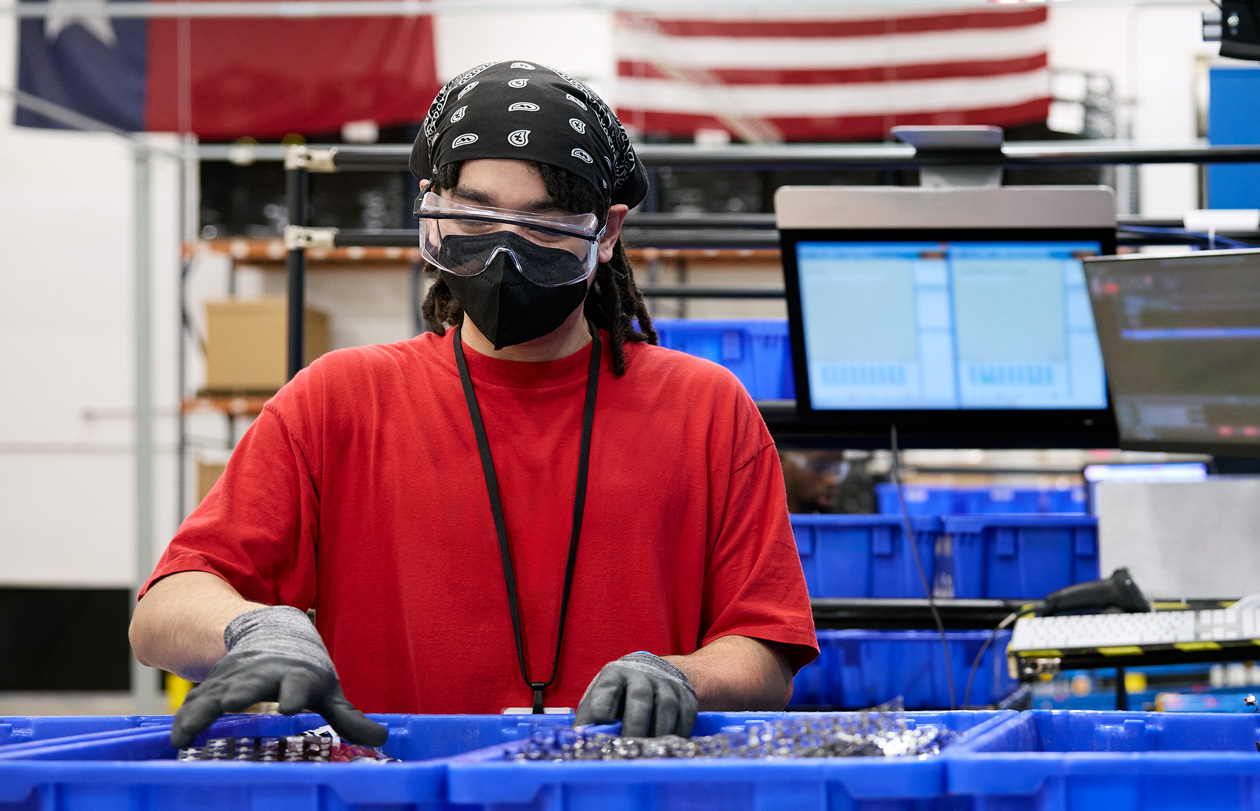 An employee wearing safety gloves, glasses, and mask handles materials at a facility