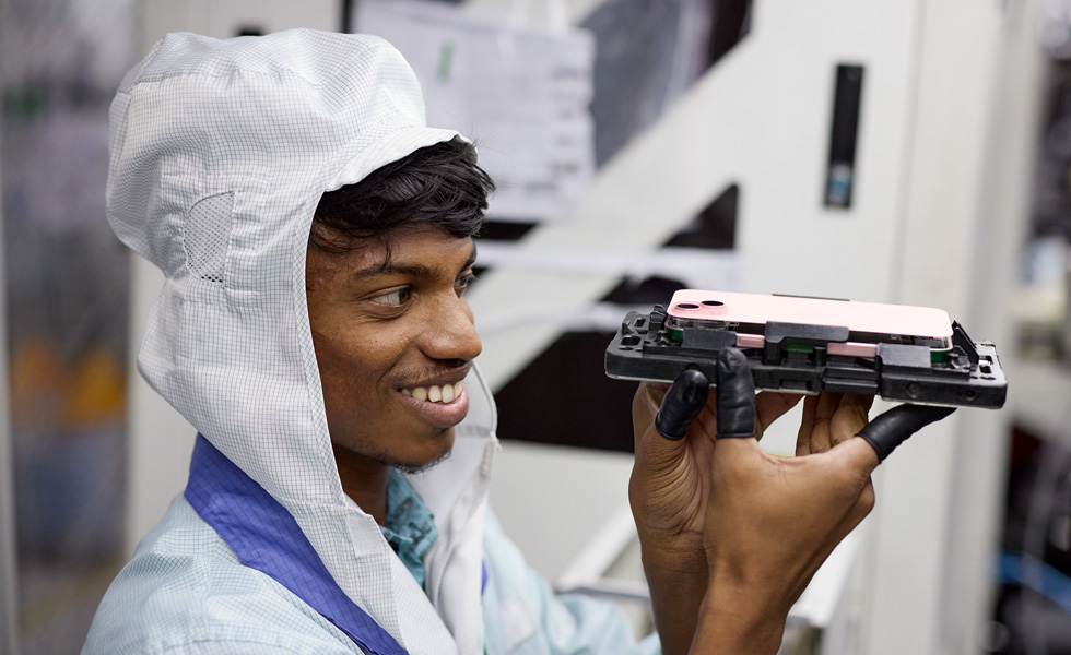 An employee in a work uniform and latex finger gloves holds up an iPhone assembly tool at eye level