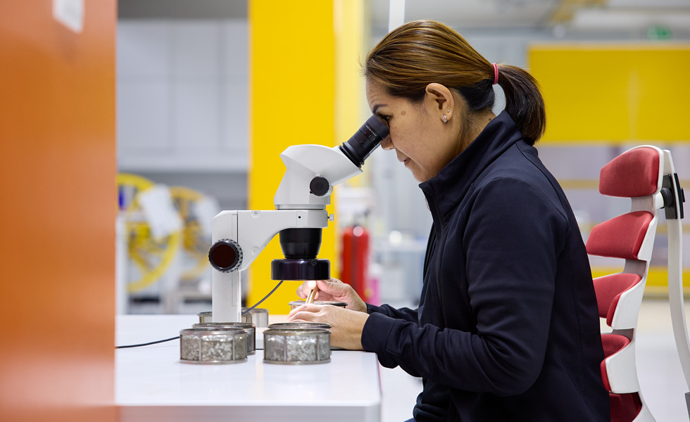 A technician inspects assembly components through a stereoscope