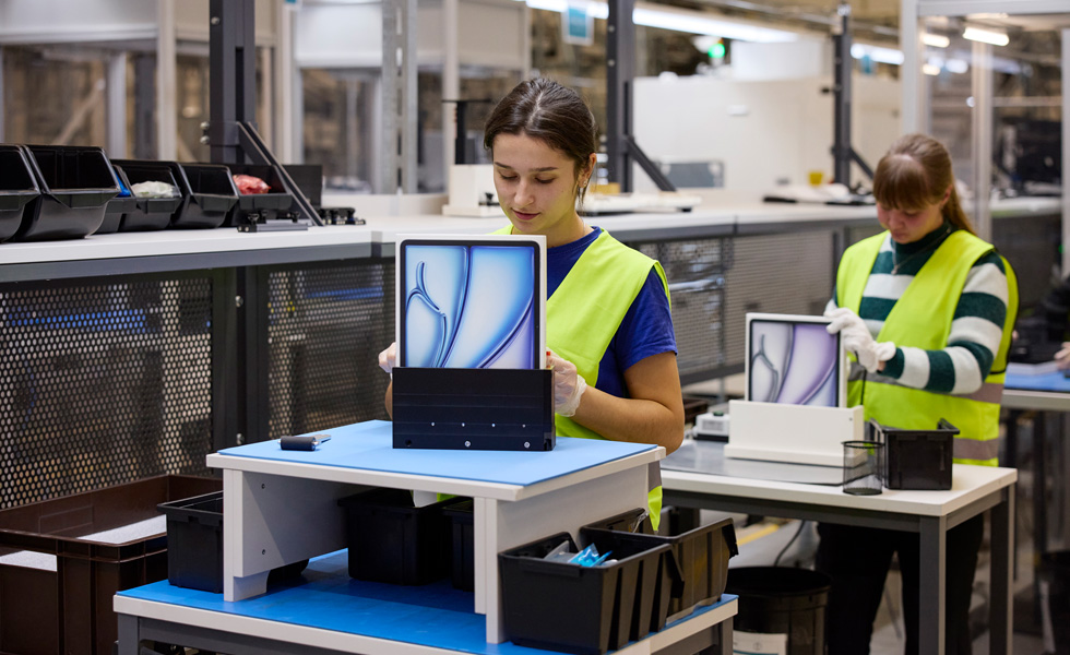 Two employees wearing high-visibility vests sit at their workstations with product packaging