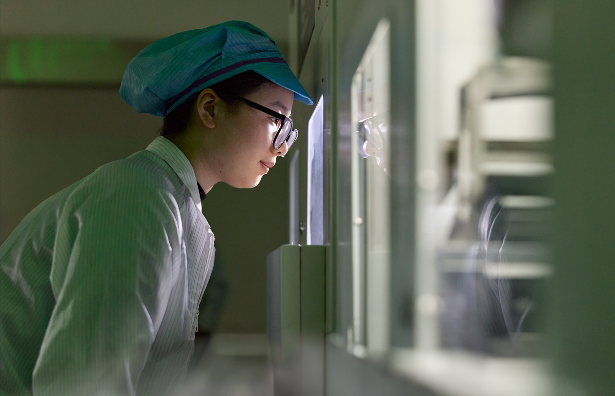 An employee in full-coverage work suit and eyewear observes Apple Watch assembly