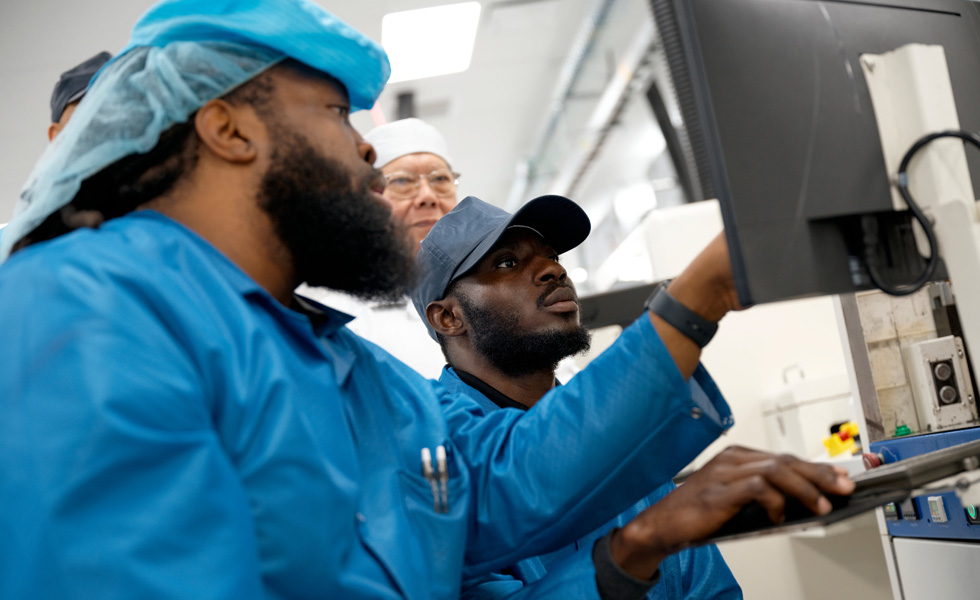 A group of employees in work suits collaborate in front of a monitor