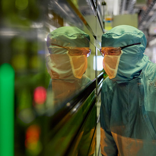 An employee in full-body work suit peers into a window of a semiconductor machine