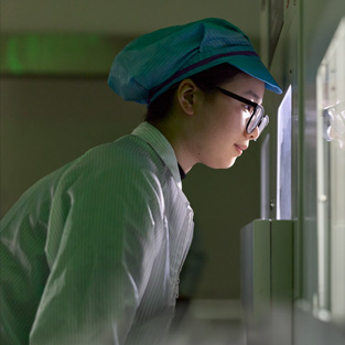 An employee in full-coverage work suit and eyewear observes Apple Watch assembly